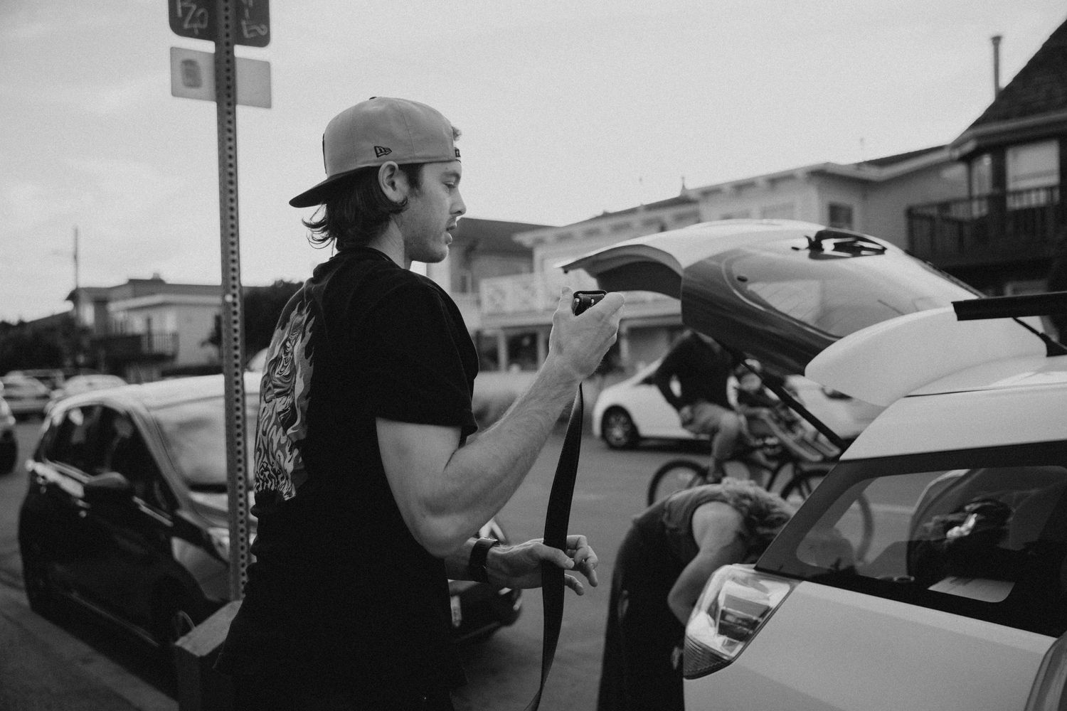 Person in black shirt and cap fueling a car at gas station.
