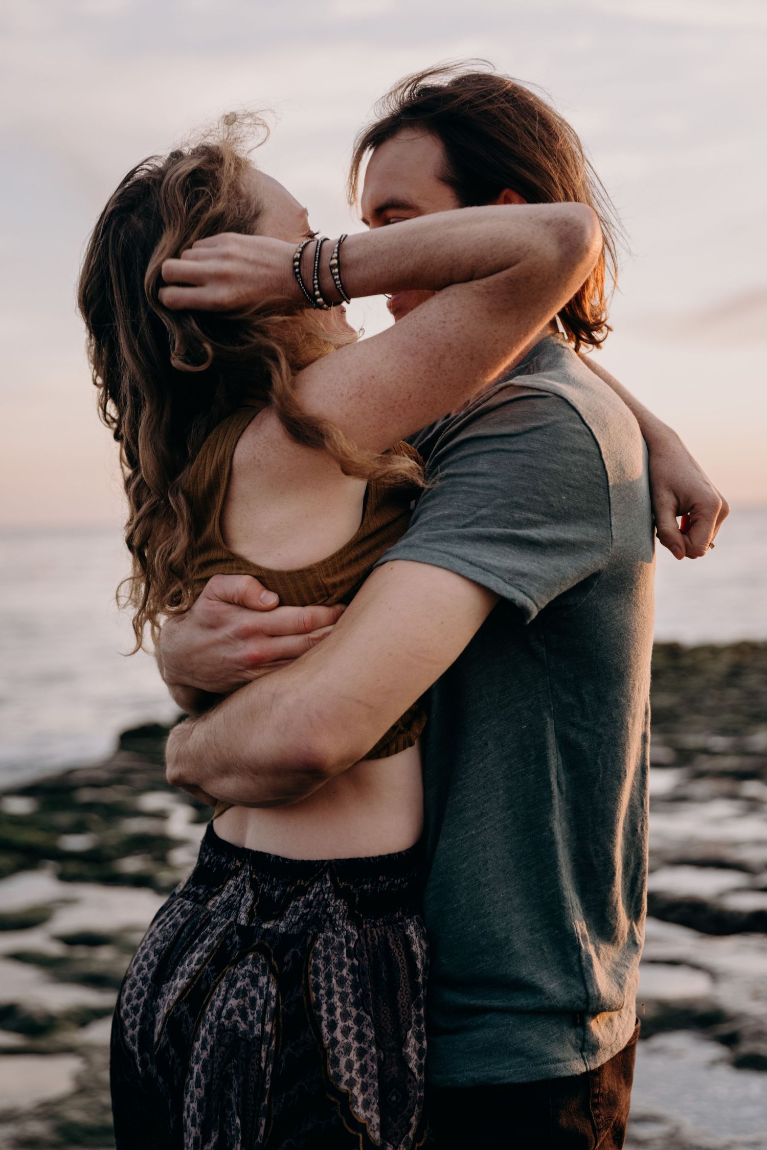 Romantic couple embracing at sunset by the ocean with warm lighting.