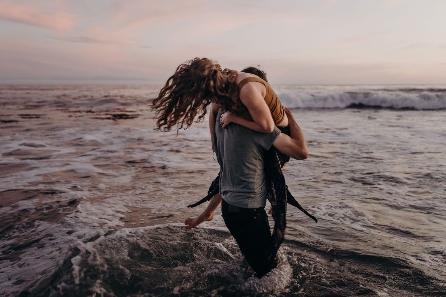 Couple embracing in ocean water during sunset with waves crashing.