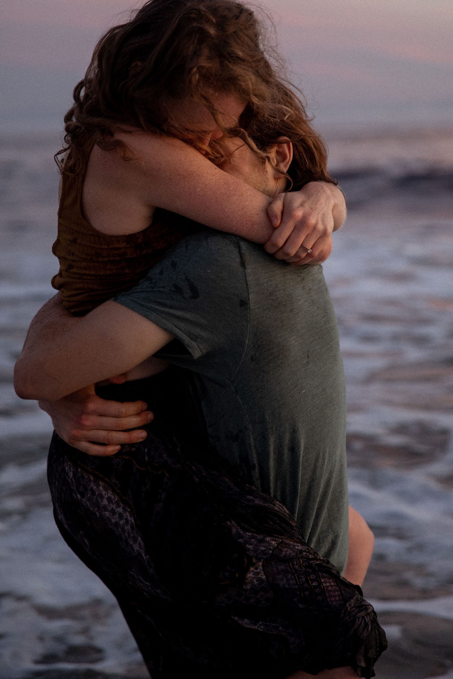 Intimate embrace on beach at sunset with ocean waves in background.