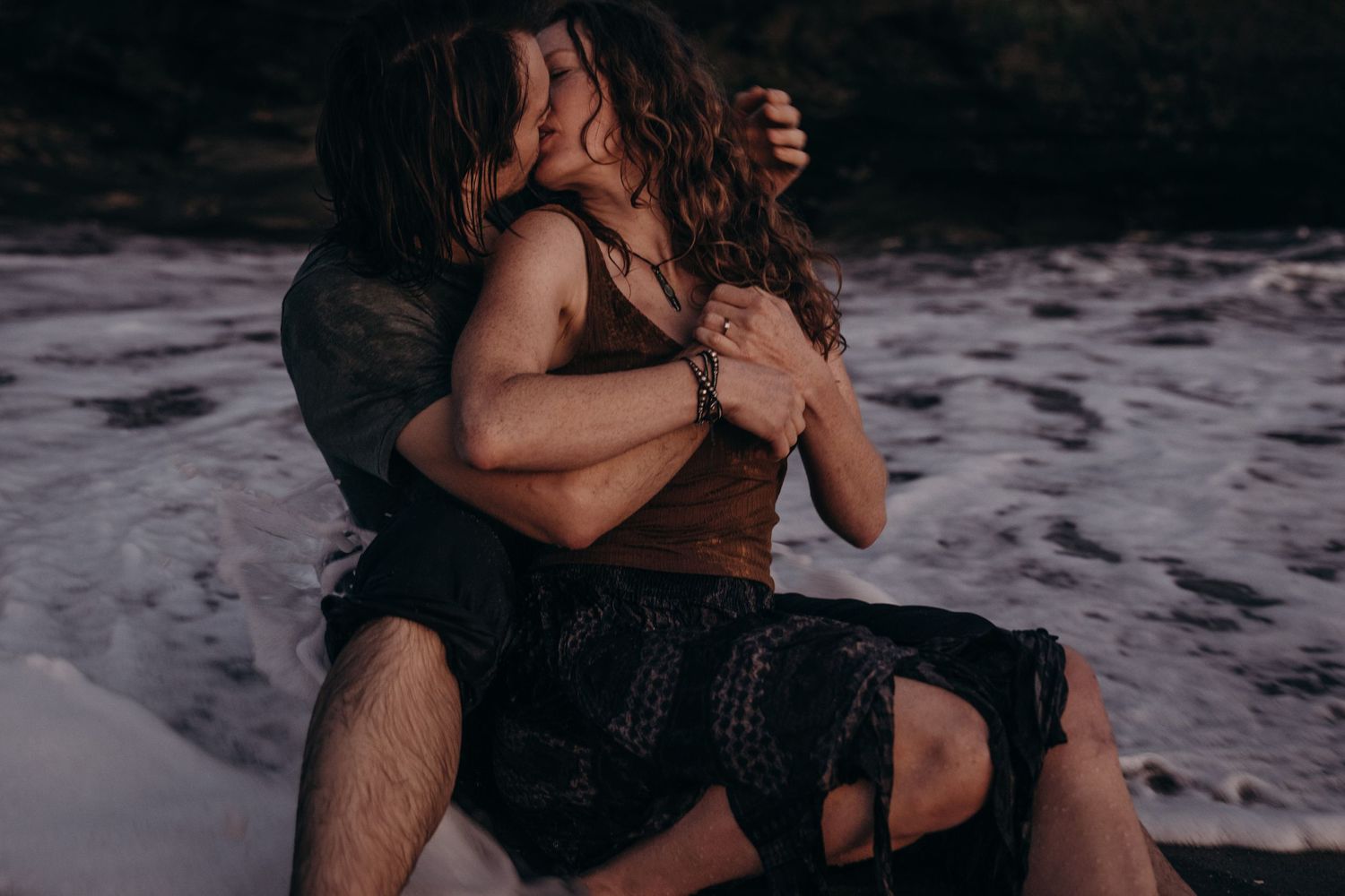 A romantic embrace in the ocean waves during purple dusk light.