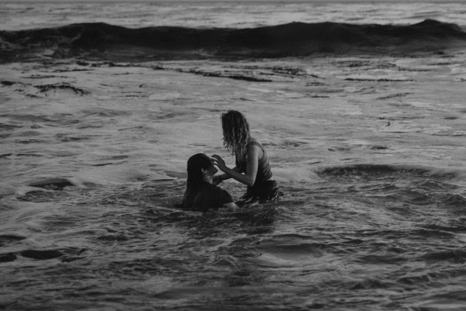 Two people embrace while sitting in dark ocean waters.