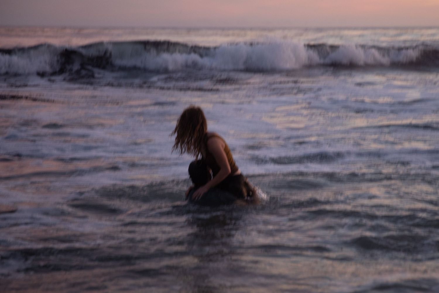 Person wading through ocean waves at sunset with breaking surf in background.