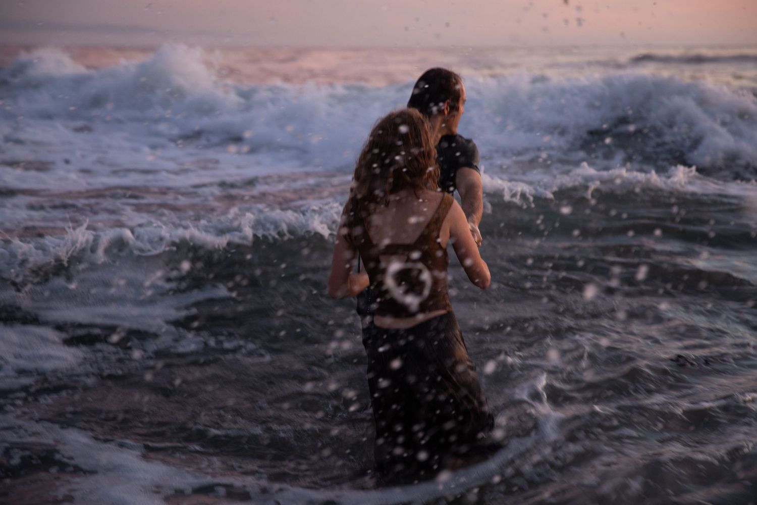 A couple sharing an intimate moment in crashing ocean waves during sunset.