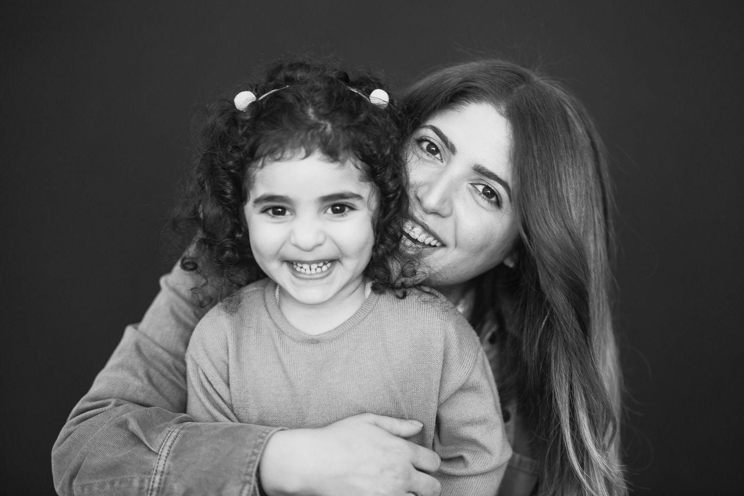 Black and white portrait of parent and child sharing joyful smiles against dark background.