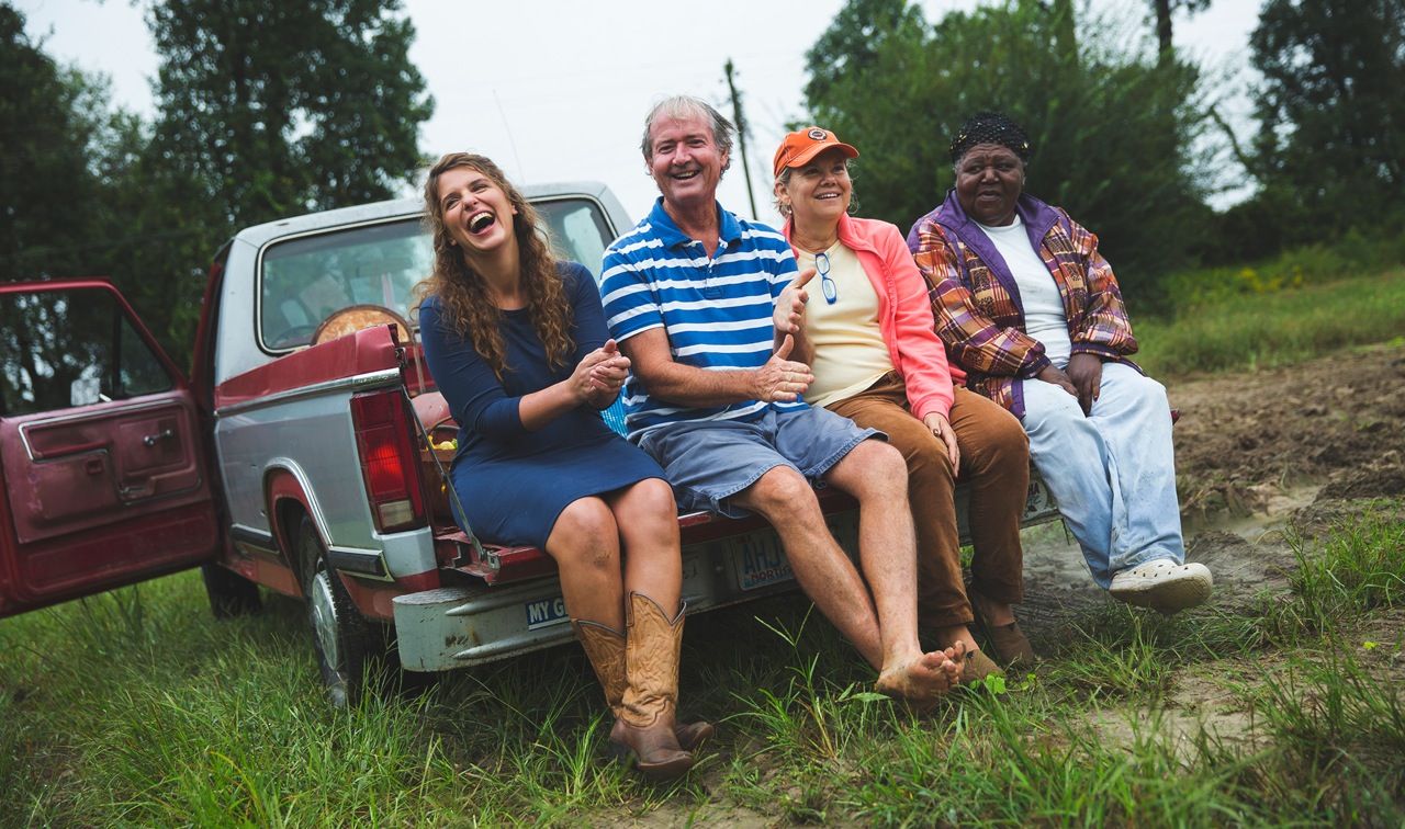 Group of friends sitting casually on the tailgate of a pickup truck in a rural setting.