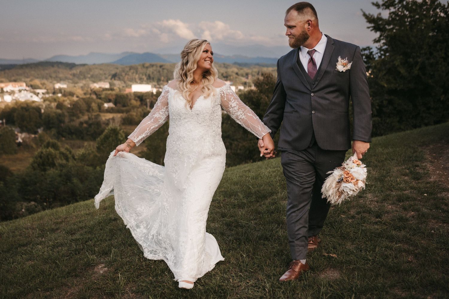A couple walks hand in hand through a scenic mountain meadow at sunset.