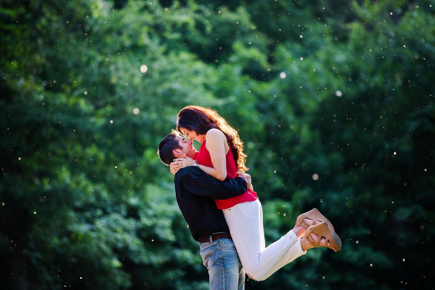 Romantic couple embracing in a playful lift pose surrounded by green foliage.