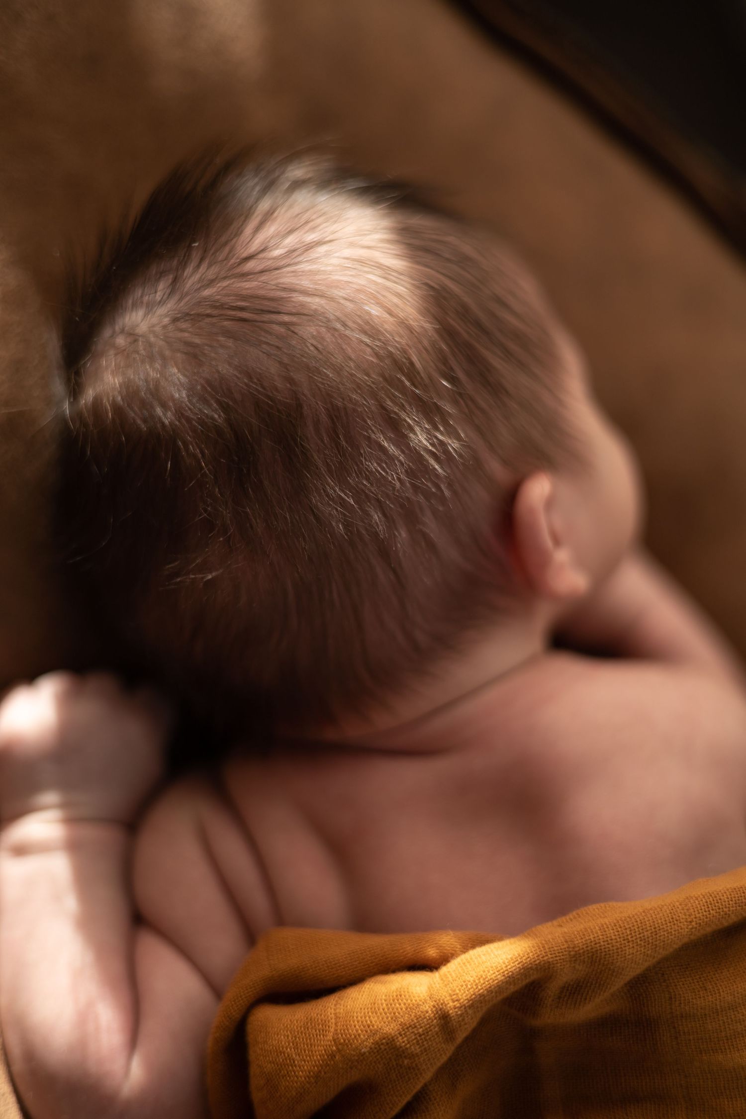 Sleeping baby wrapped in cozy orange blanket in natural light setting.