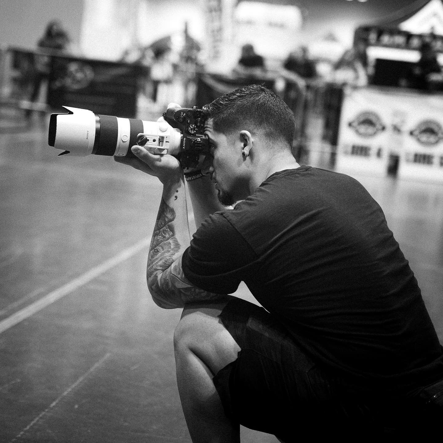 Photographer with tattoos crouching down while shooting with a telephoto lens.