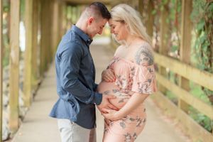 Intimate maternity photo of couple embracing on wooden bridge surrounded by greenery.