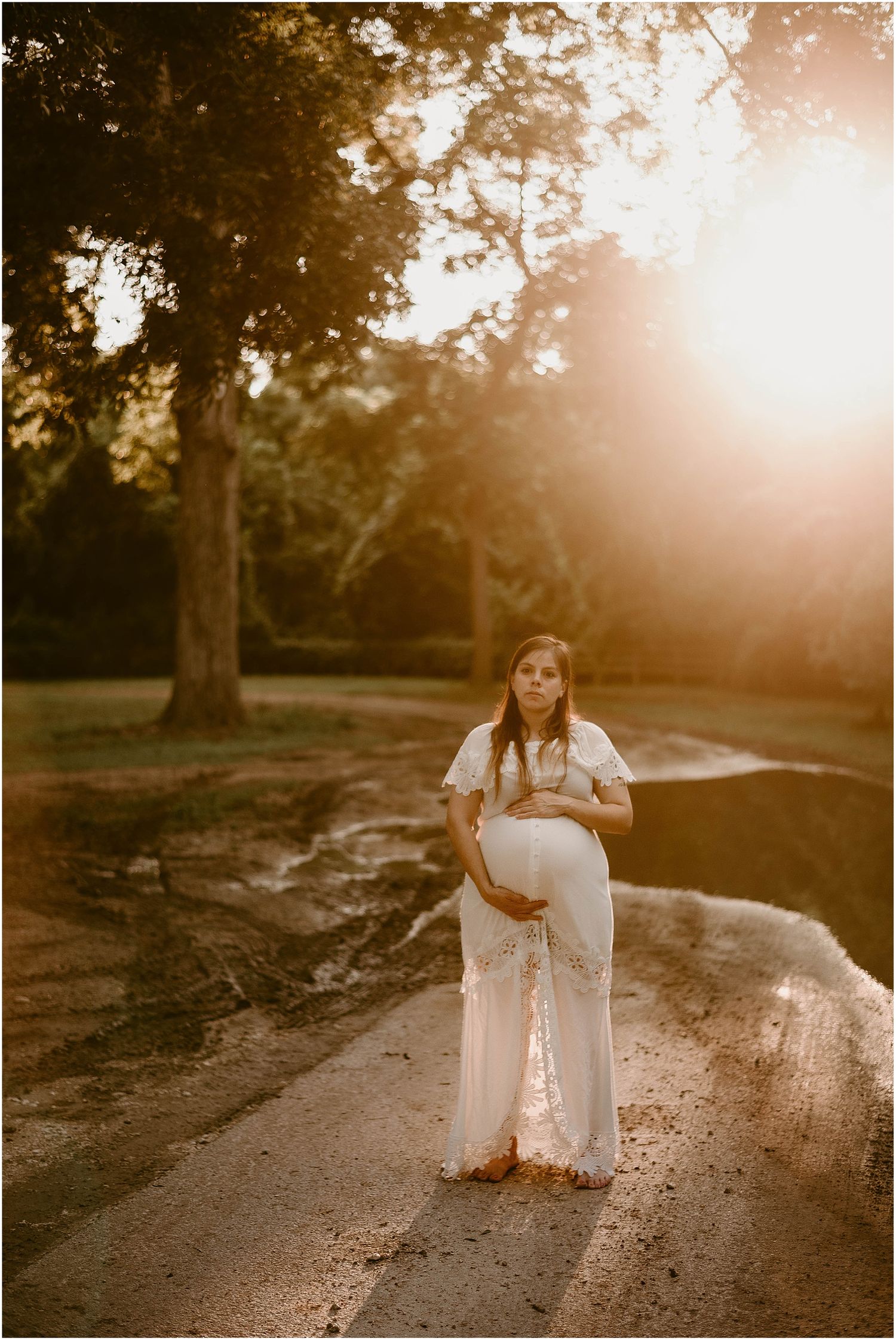 Full-length maternity portrait in white lace dress during sunset.