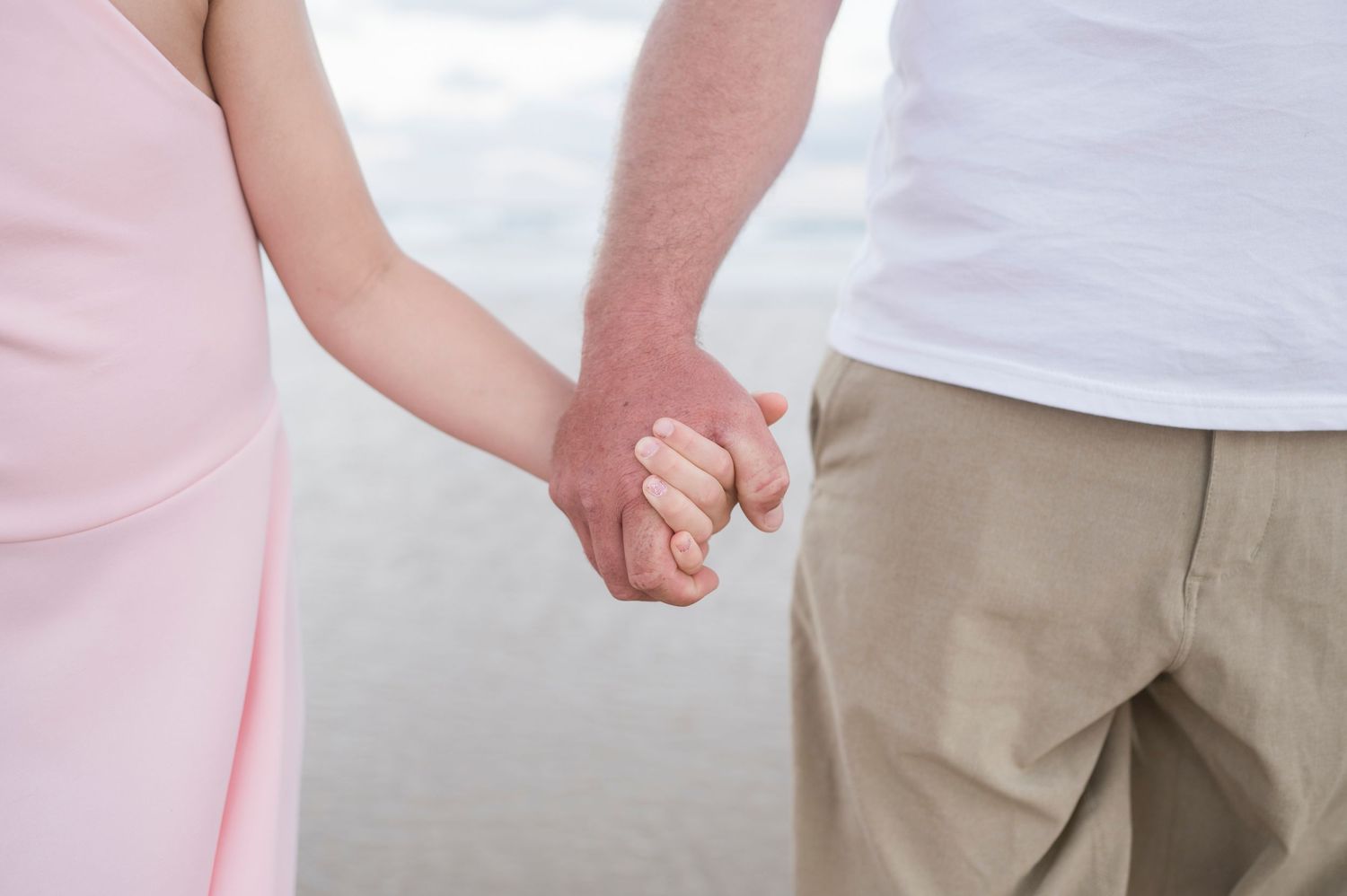 A close-up shot of two people holding hands while wearing pink and neutral colored clothing.