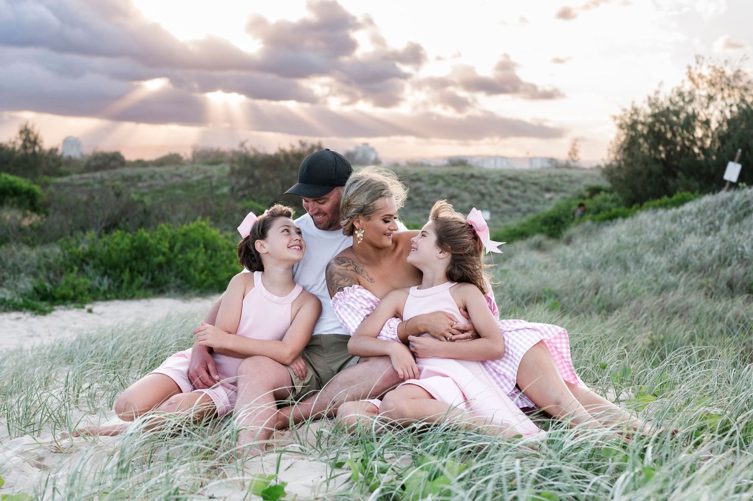 A joyful group sits together in a grassy field during sunset wearing coordinated pink outfits.