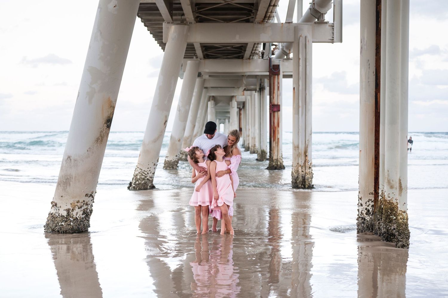 A group walks under a beach pier while wearing matching pink outfits.