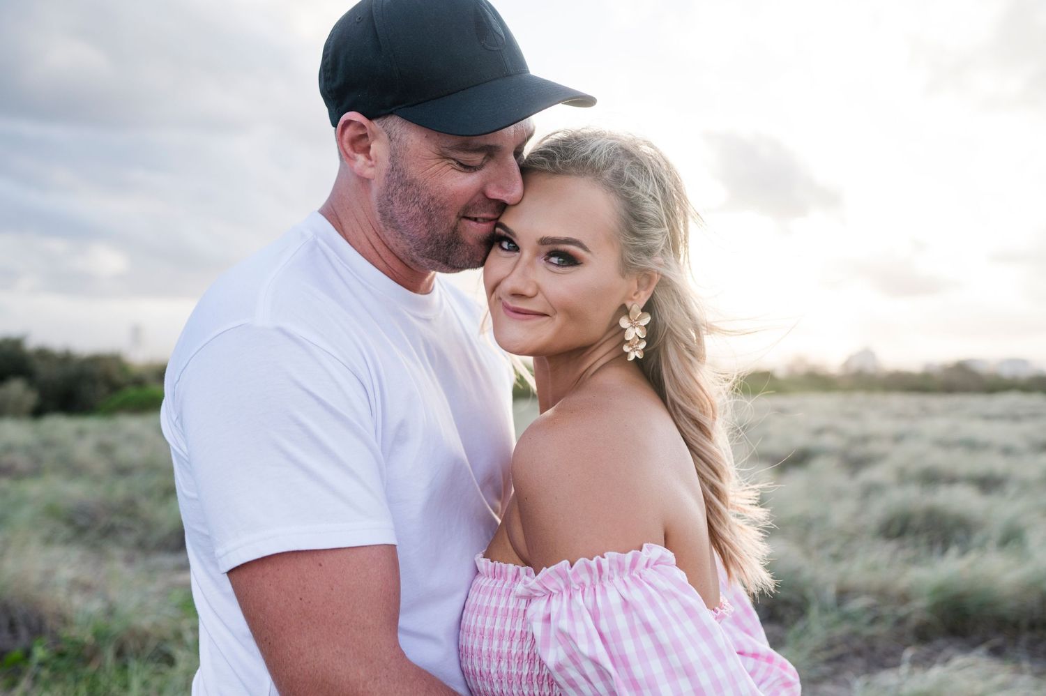 A romantic couple embraces on a grassy hill during golden hour.