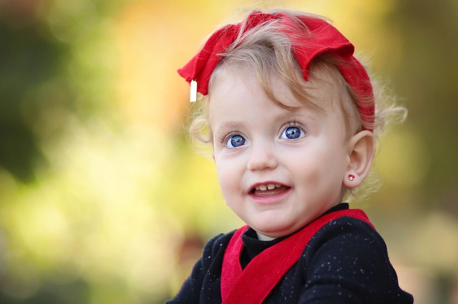 A close-up portrait showing bright blue eyes and red accessories against a blurred natural background.
