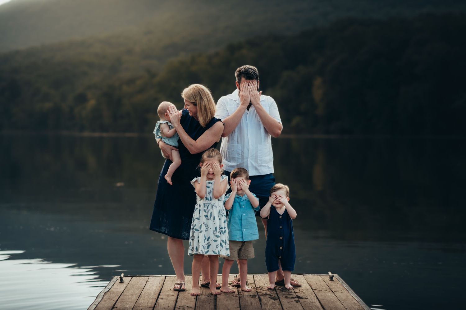 family of 6 all play peekaboo together at family photo session. all have hands covering eyes.