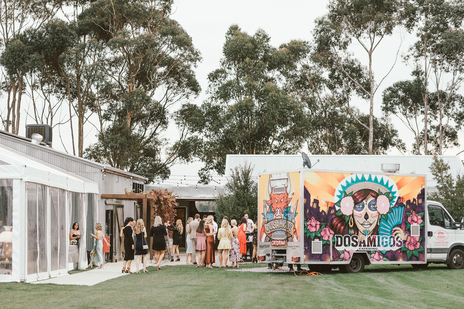 White wedding tent setup with a colorful food truck and tall eucalyptus trees in the backdrop.