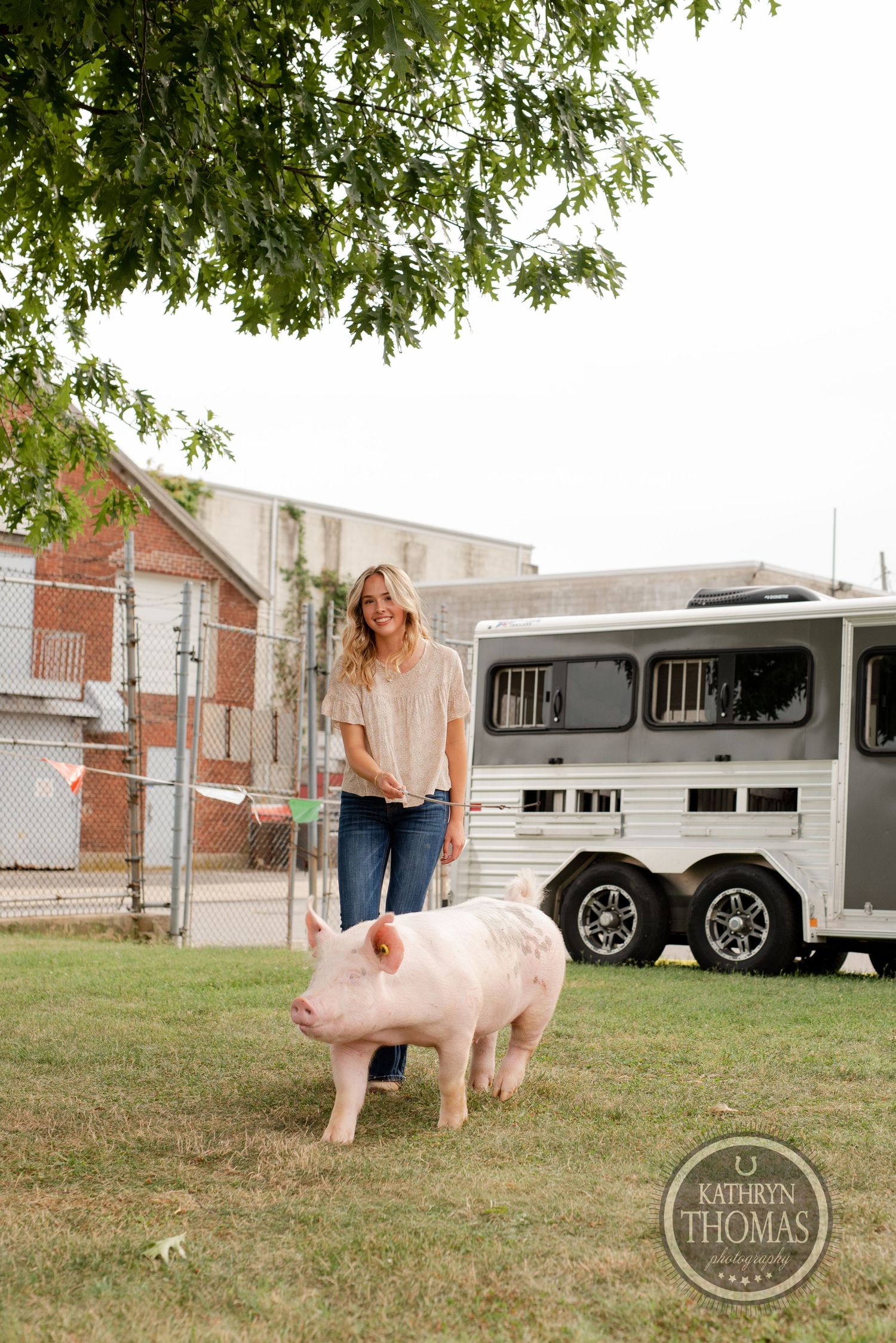 A pink pig stands near a horse trailer on grass with someone in casual attire nearby.