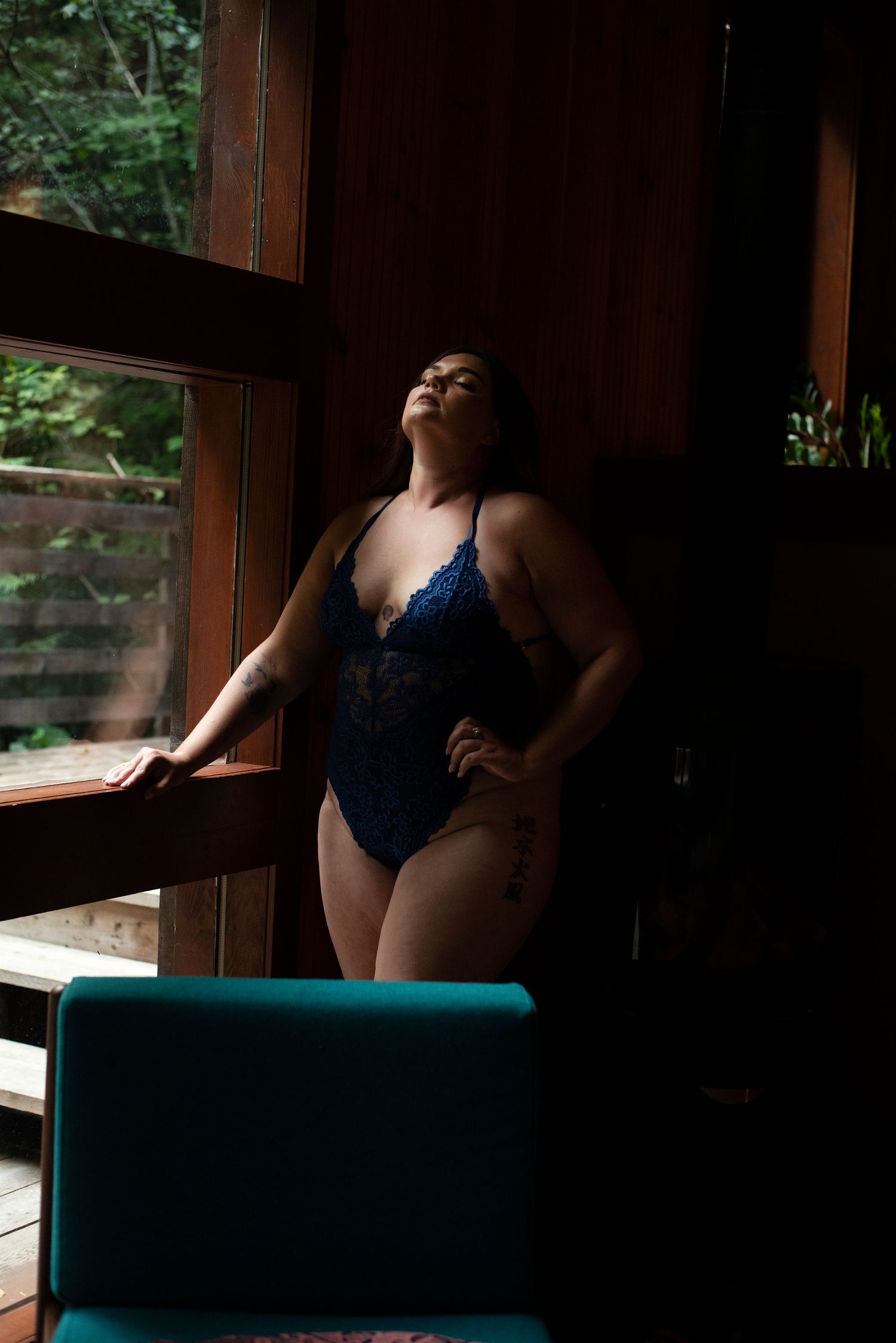 Natural window light creates dramatic shadows on navy blue bodysuit.