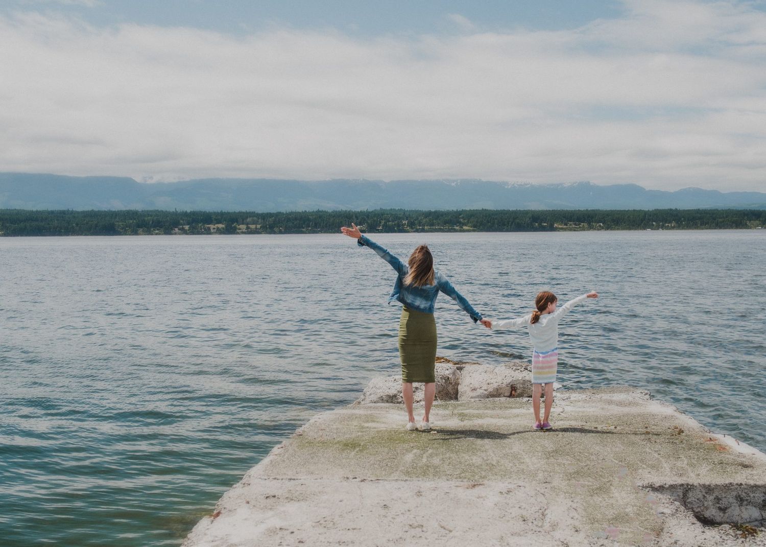 Woman and dog playing joyfully on a concrete pier overlooking a serene lake.