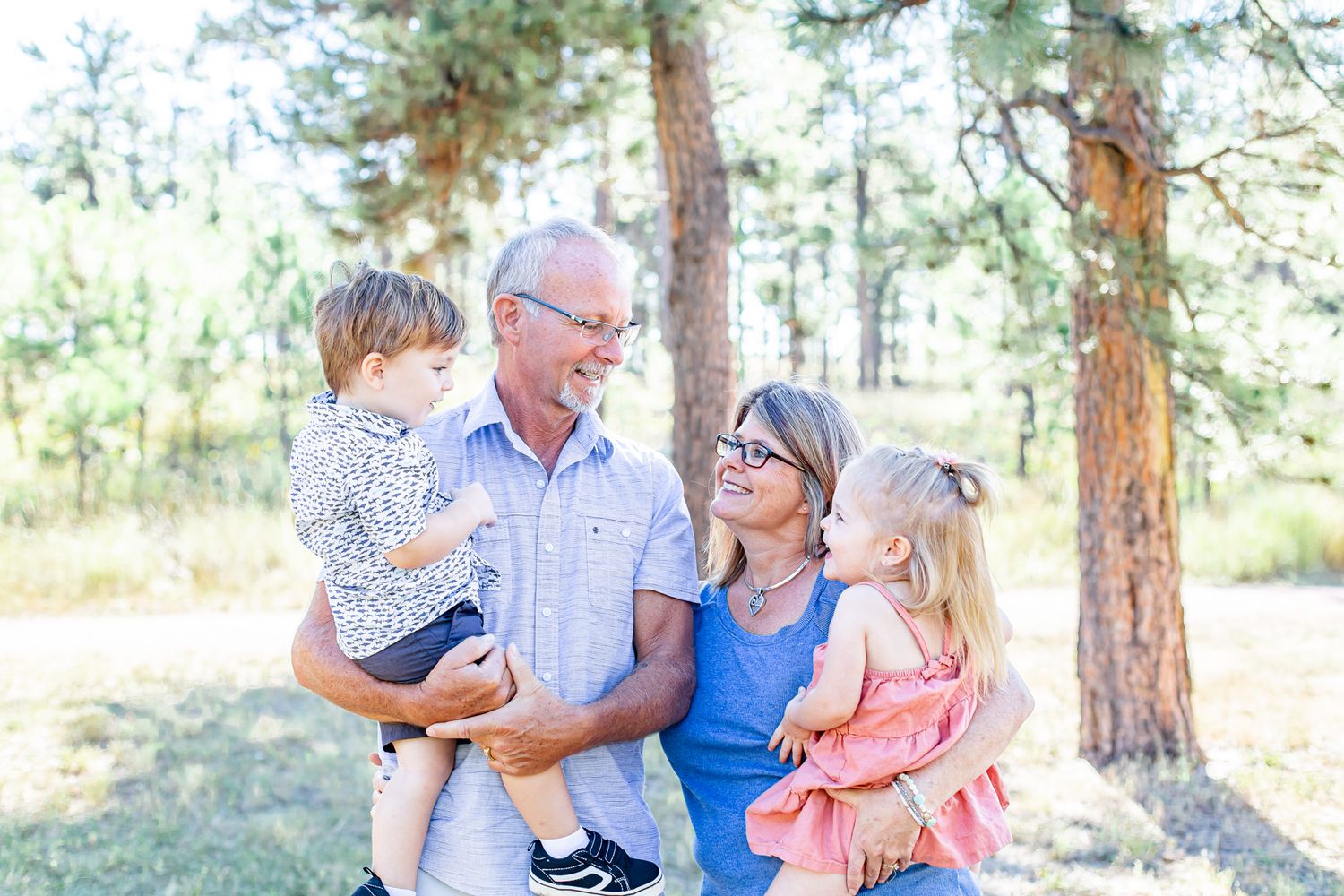 Grandparents holding their two toddler grandchildren smile at each other in Black Forest, Colorado.