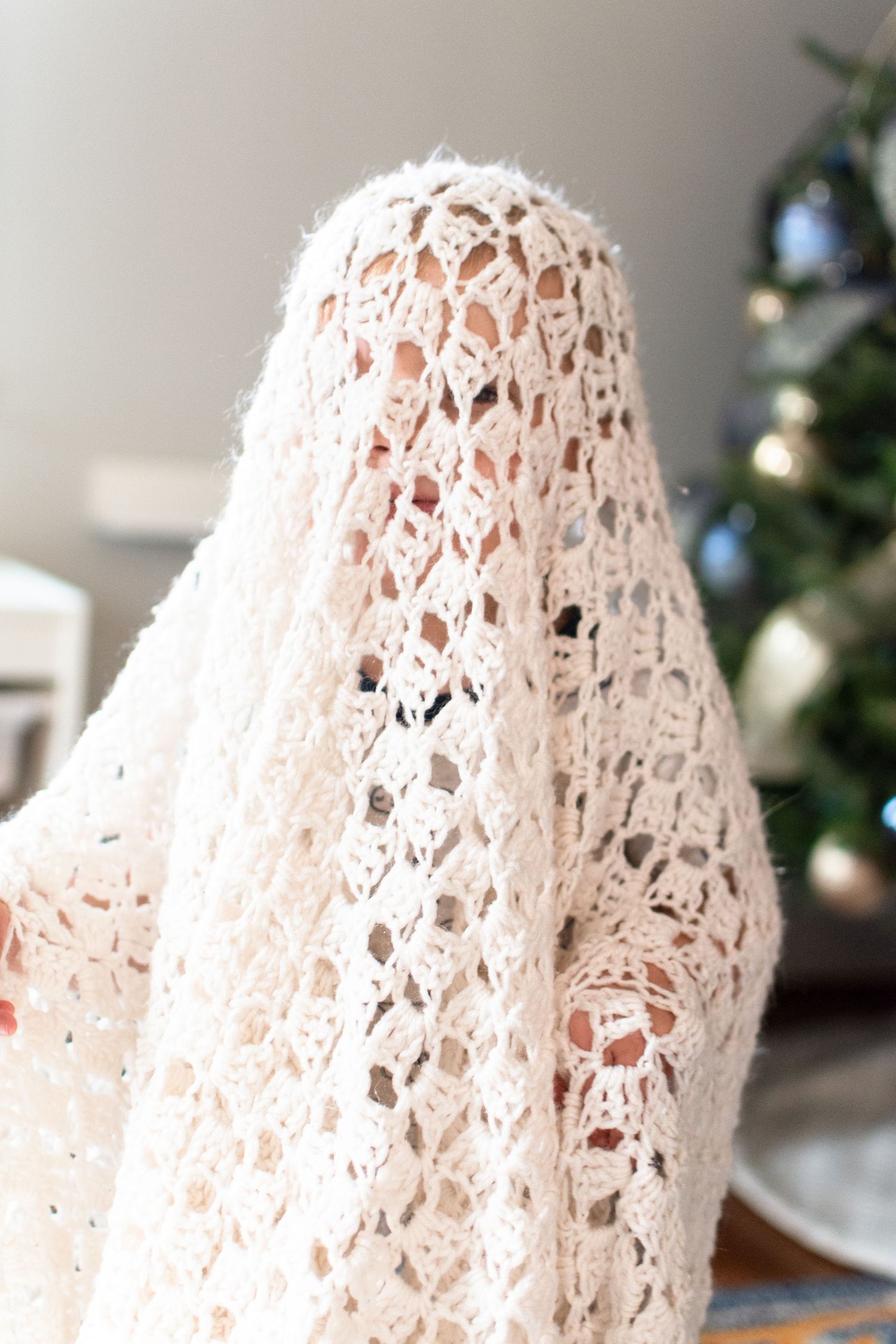 A toddler pretends he is a ghost in a crocheted blanket made by his great-grandmother.