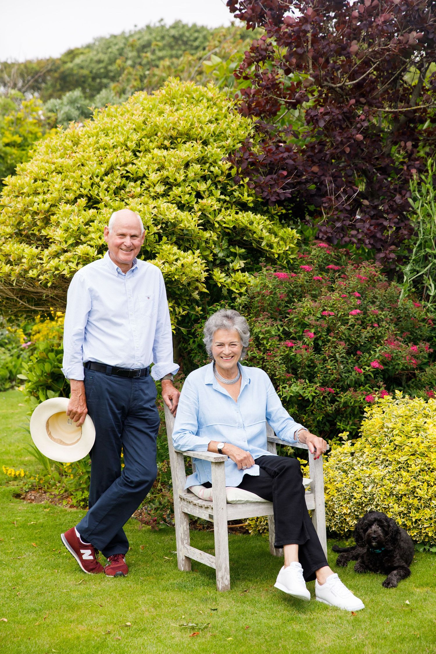 Elderly couple and small dog relaxing in their lush backyard garden.