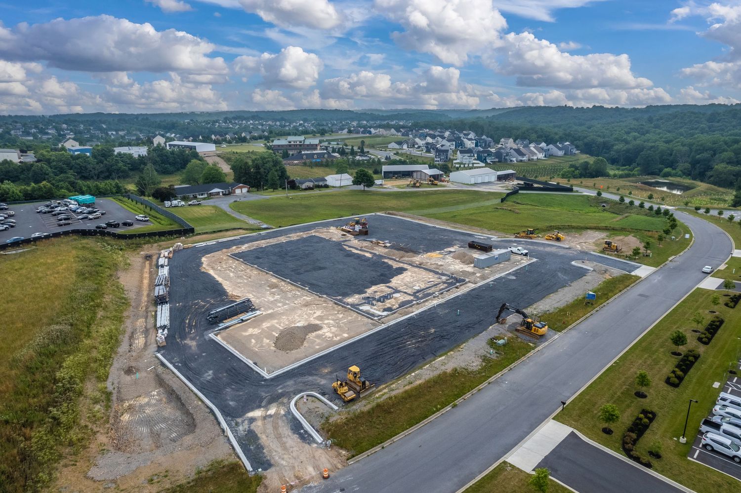 Construction site with concrete foundation and paved roads in a developing suburban area viewed from above.