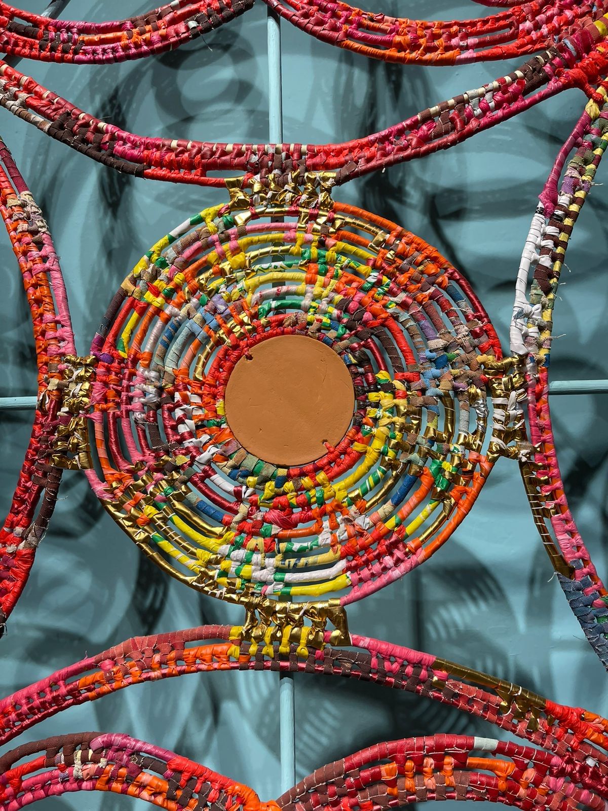 Detailed mosaic pattern with concentric circles in red, yellow and orange on teal background.