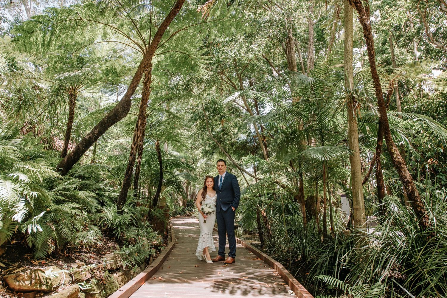 Romantic garden wedding photo on a lush green path surrounded by tropical foliage.