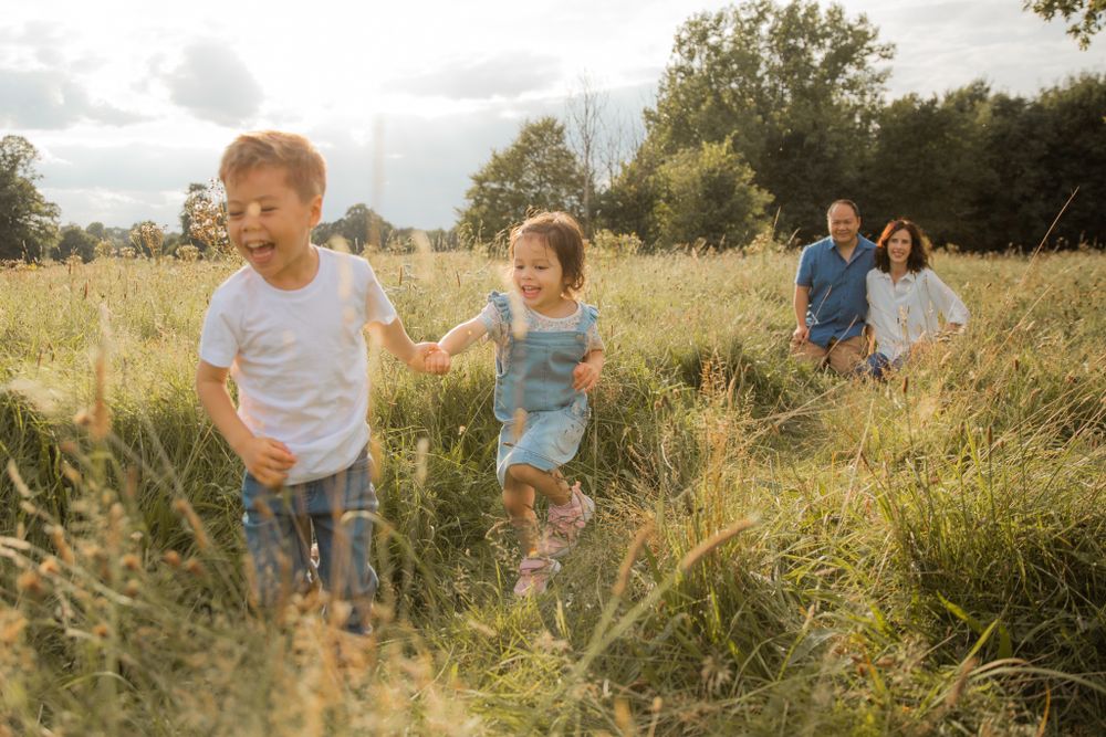 Family running playfully through tall grass field at sunset.