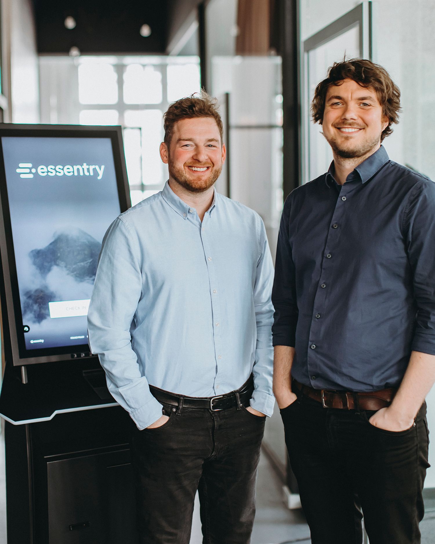 Professional team members in business attire stand together in an office hallway with the Essentry logo visible.
