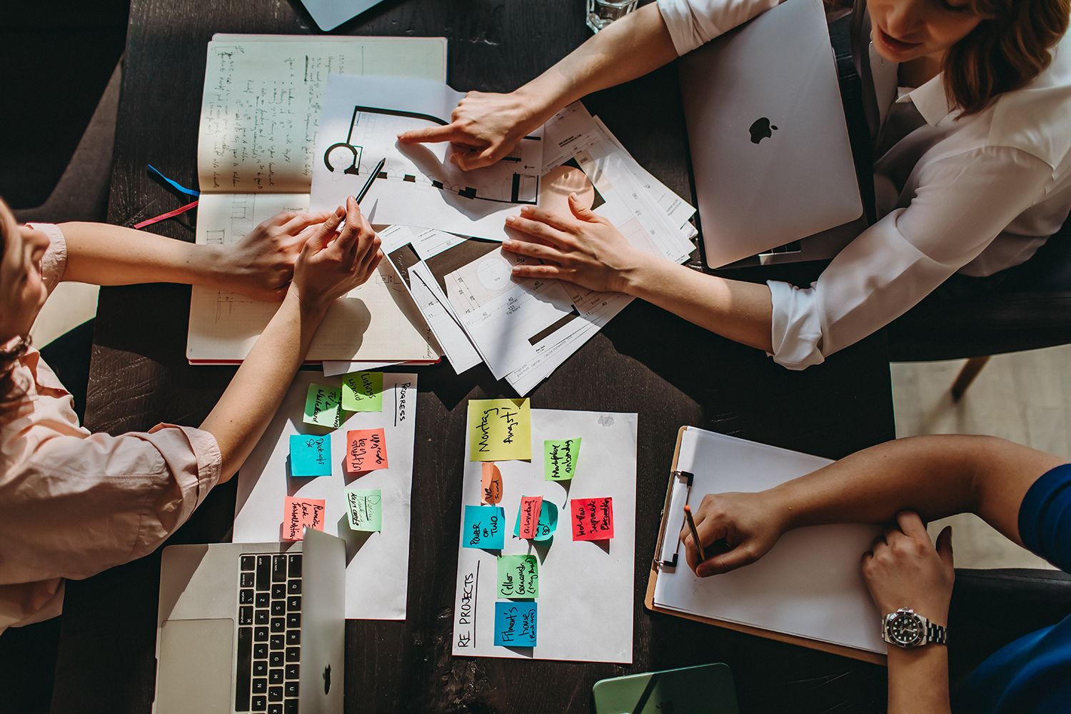Overhead view of hands collaborating on colorful sticky notes during a business meeting.