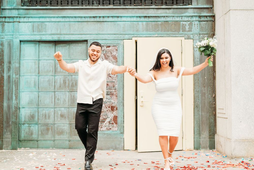 A joyful couple poses against a turquoise door with rose petals scattered at their feet. New York City