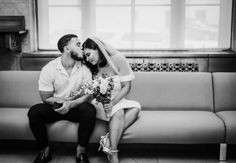 A casual engagement photo of a couple sharing a tender moment on a couch.