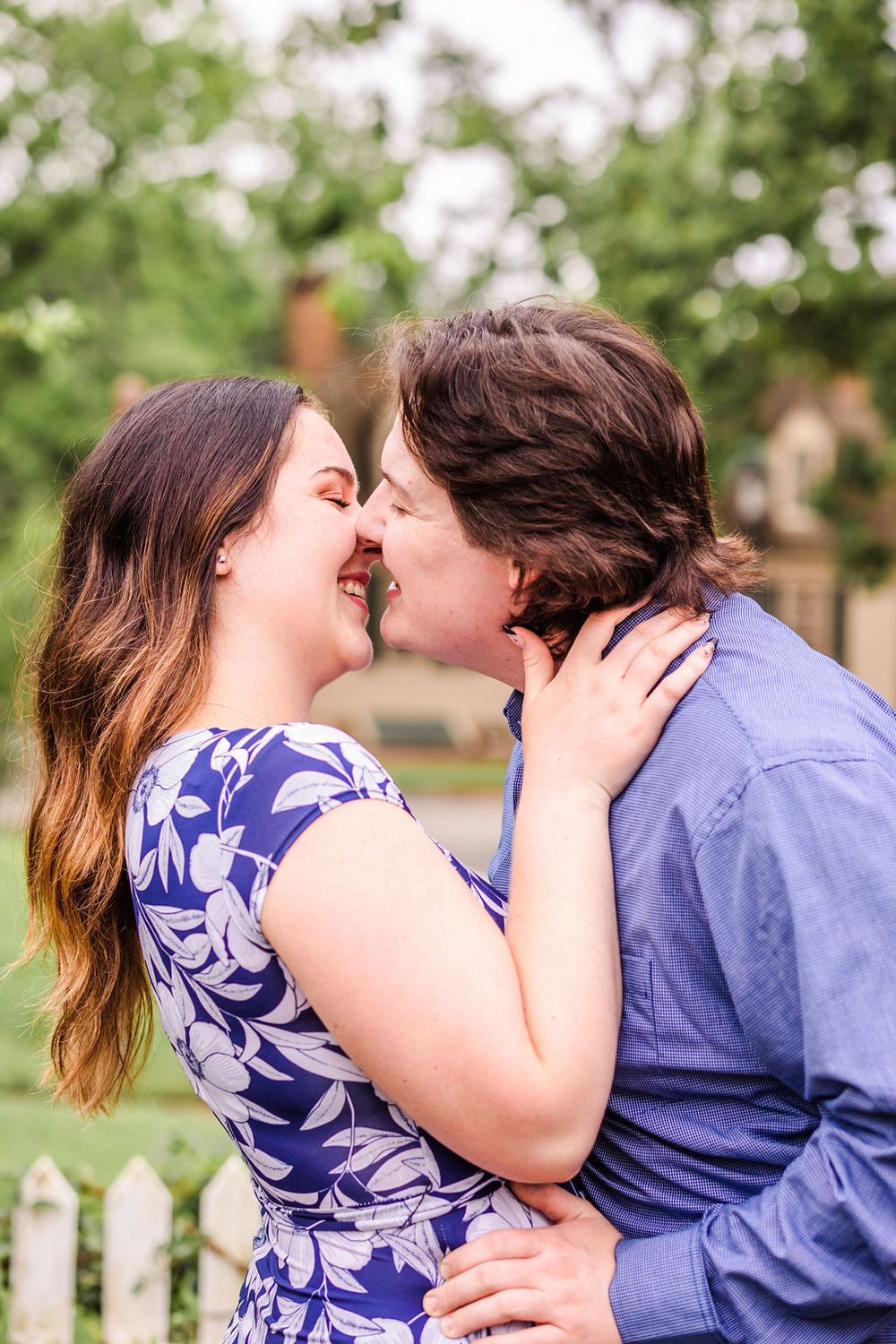 A romantic kiss between a couple in a blue dress and shirt against a garden backdrop.