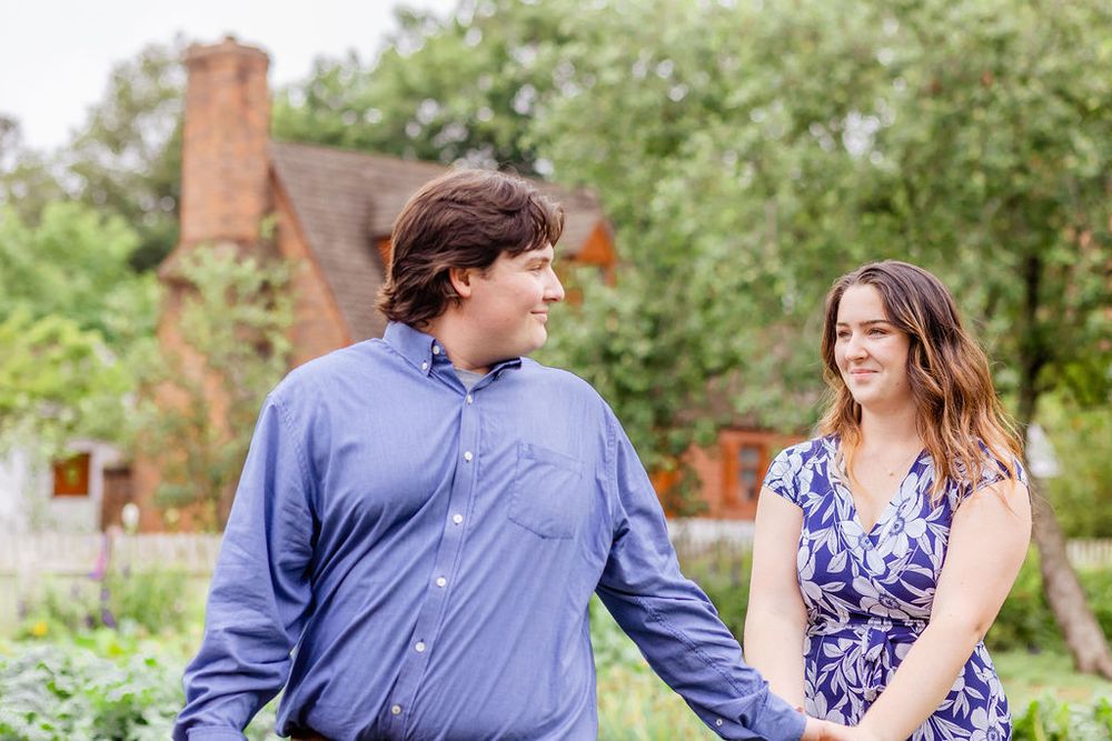 A couple in matching blue outfits share a tender moment in front of a brick house.