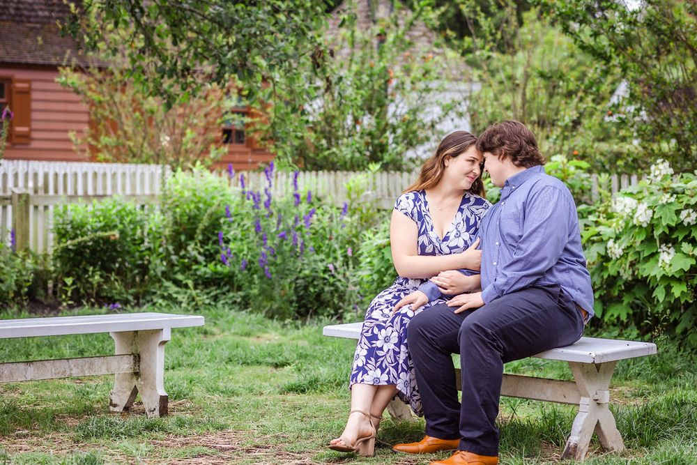 A couple shares an intimate moment while sitting on a wooden bench in a garden setting.