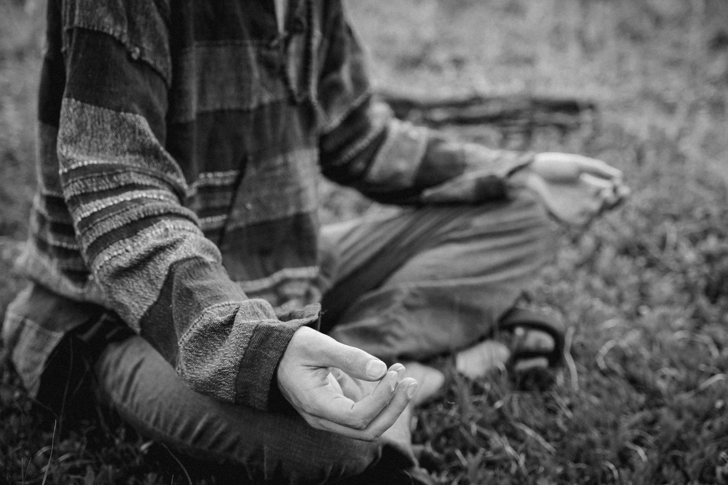 Black and white close-up of hands in meditation pose on ground.