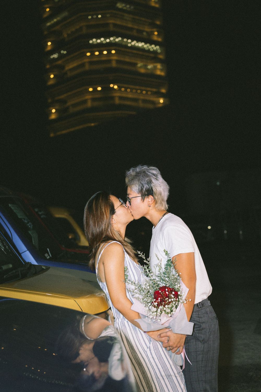 A tender moment captured at night with a lit building creating a romantic backdrop.