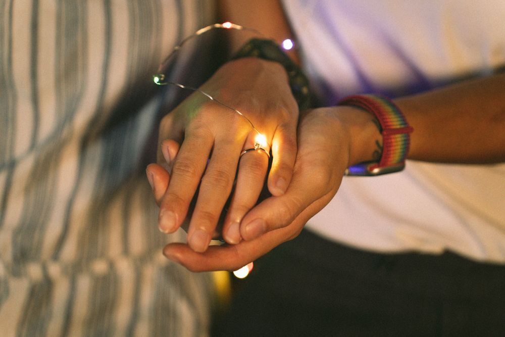 Two hands clasped together in romantic lighting with a ring visible.