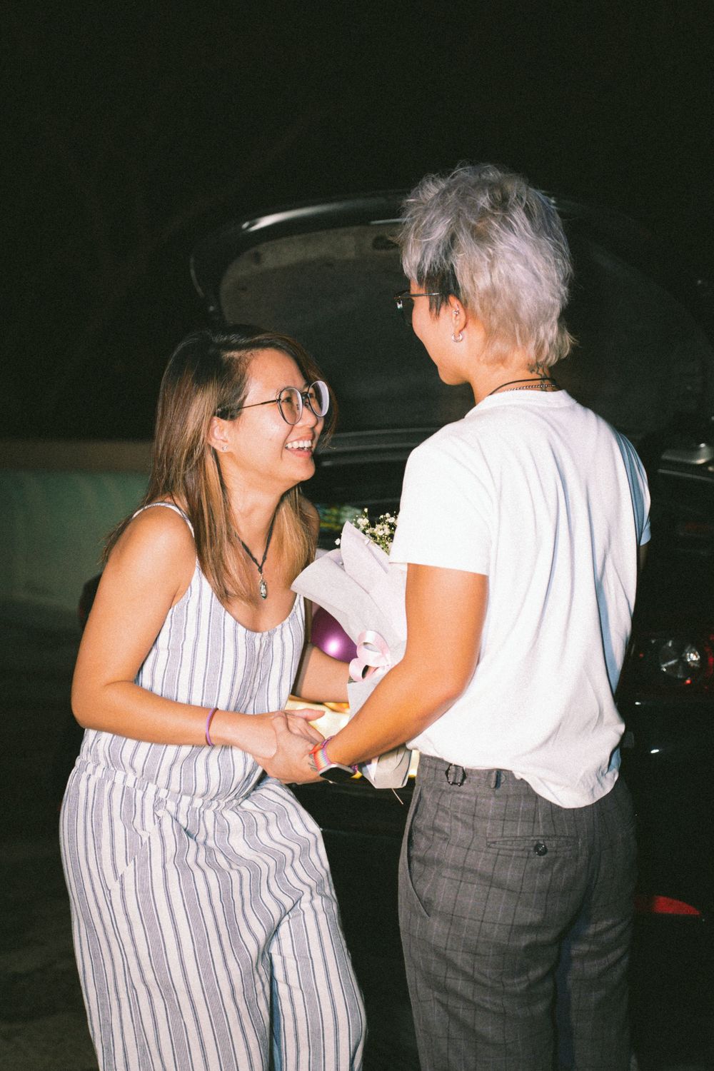 A romantic nighttime moment between two people near a decorated car trunk.