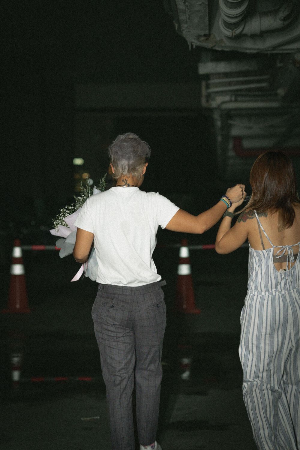 Two people walking away from camera at night holding flowers.