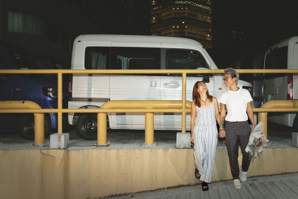 Two people walking together at night with a white van and illuminated building in the background.
