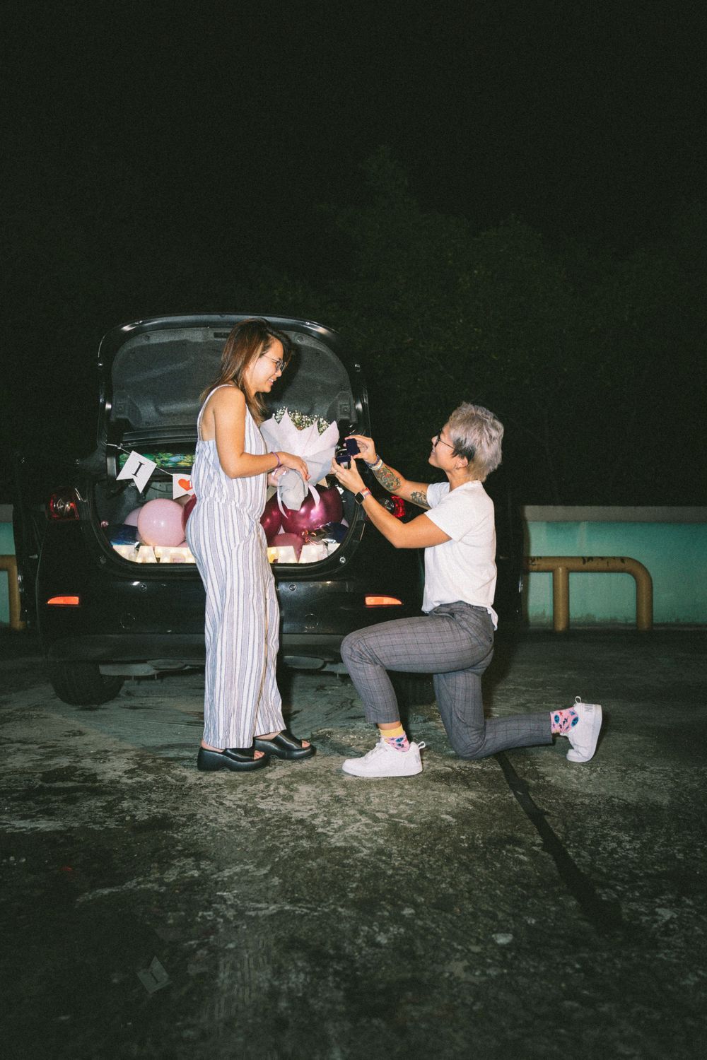 A romantic proposal scene at night with a decorated car trunk in the background.
