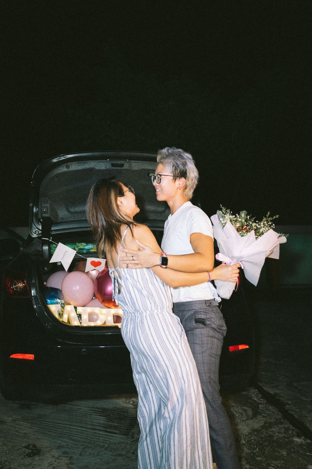 A romantic nighttime scene by a car trunk with flowers and a striped dress against a dark background.
