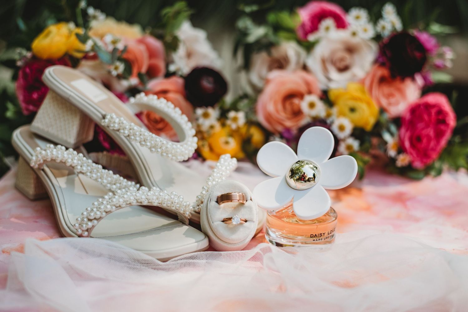 Wedding accessories including bridal shoes and perfume arranged with pink and yellow roses.