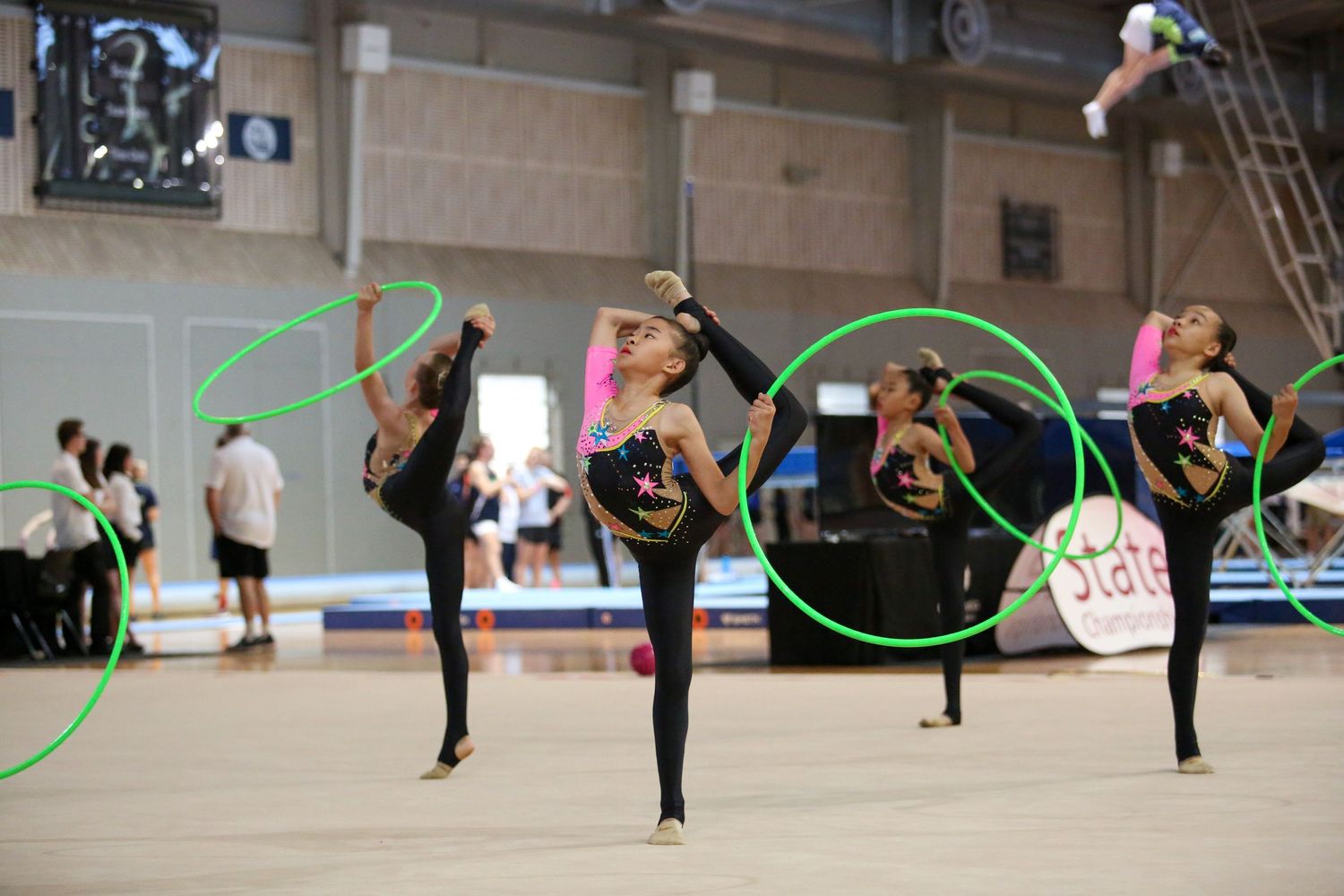 Rhythmic gymnasts perform with green hoops in synchronized formation during competition.